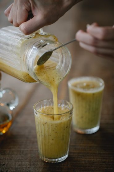 person pouring smoothie into a drinking glass